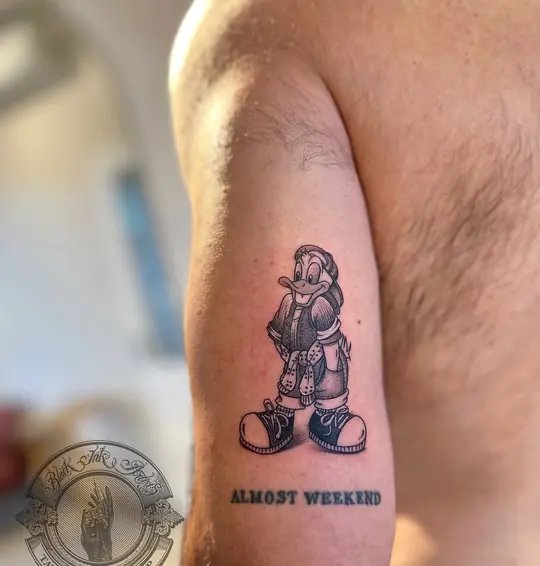 Cartoon character tattoo with lettering on arm